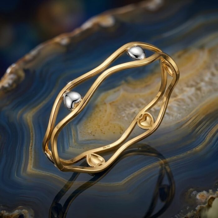 ⁦اسورة فاخرة باللون الذهبي الأنيق، بتصميم مموج ومزدوج، تتزين بقلوب رقيقة باللون الفضي اللامع. قطعة عصرية تضفي جاذبية لإطلالتك.⁩ - الصورة ⁦7⁩